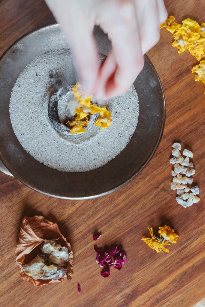 Eine Hand legt Räucherwerk auf eine glühende Kohle auf.